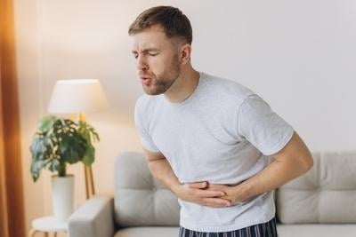 Young man clutching stomach, showing discomfort indoors
