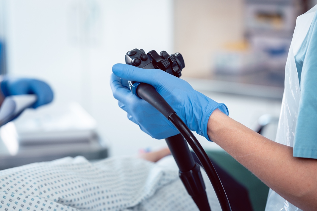 Max-gen-exerpertise 1 | Akron Digestive Health Gloved medical professional holding a flexible endoscope above a patient on an exam table in a clinical setting.
